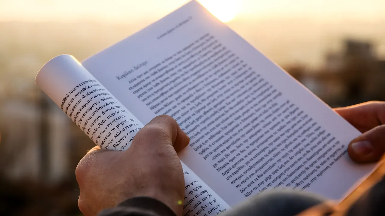 A hand holding a page of Greek text in warm evening light
